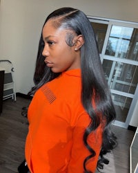 a black woman wearing an orange shirt with long wavy hair